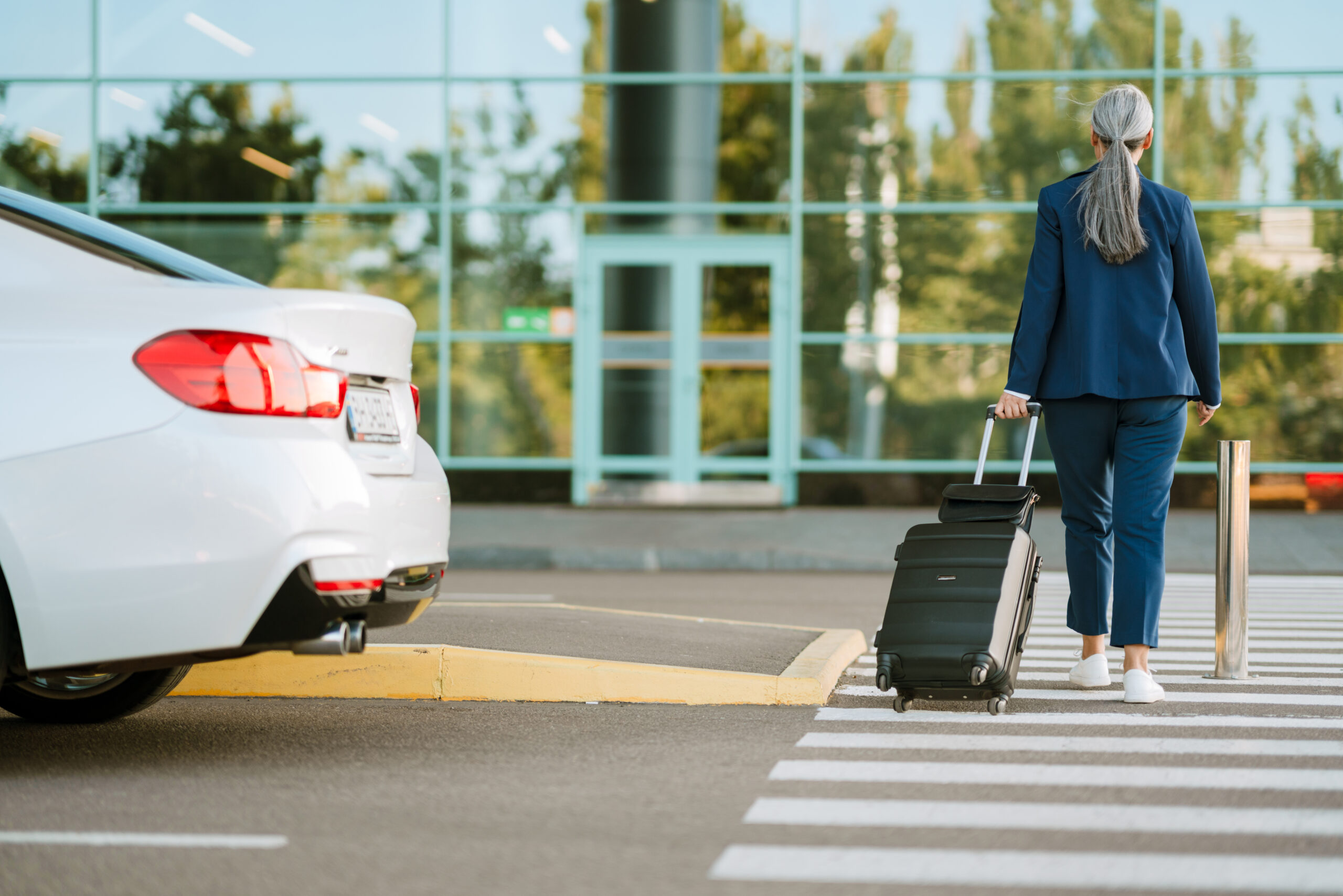Grey woman walking with suitcase on road by airport outdoors